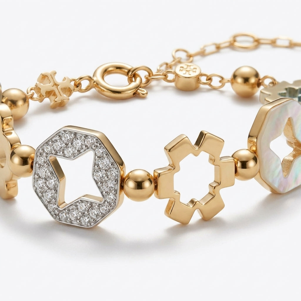 A gold-toned bracelet featuring geometric star-shaped charms, a pavé-set clear stone octagonal charm, and an iridescent shell inlay, photographed on a clean light gray background.