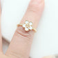 A gold ring with a white enamel four-petal flower face, worn on a finger against a clean white background.