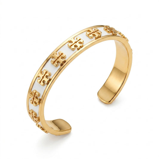 A gold-plated cuff bracelet featuring a repeating white enamel inlay with embossed gold monogram motifs, shown on a clean white background.