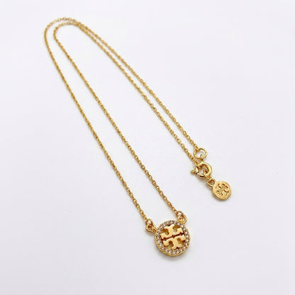 A gold chain necklace featuring a circular pendant with a gold 'T' logo surrounded by small clear crystals, and a small round tag charm, displayed on a clean white background.