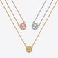 Three circular pendant necklaces on chains, shown on a light gray background. The necklaces are in yellow gold, rose gold, and silver tones, each featuring a pavé-set circular logo pendant with a central letter design.