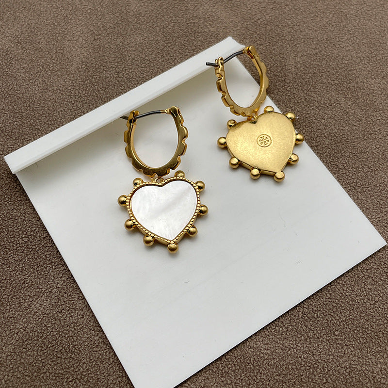 Close-up of one earring, highlighting the texture of the gold heart and the iridescent, smooth surface of the mother of pearl teardrop.