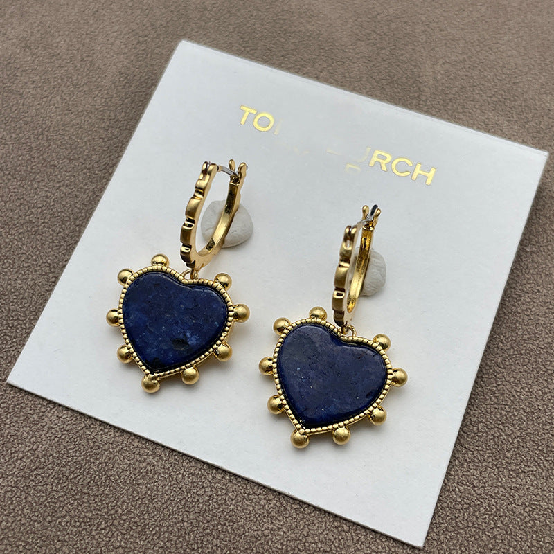 Both earrings laid side-by-side on a soft, neutral background (light gray velvet), showcasing the heart charm and mother of pearl drop in clear detail.