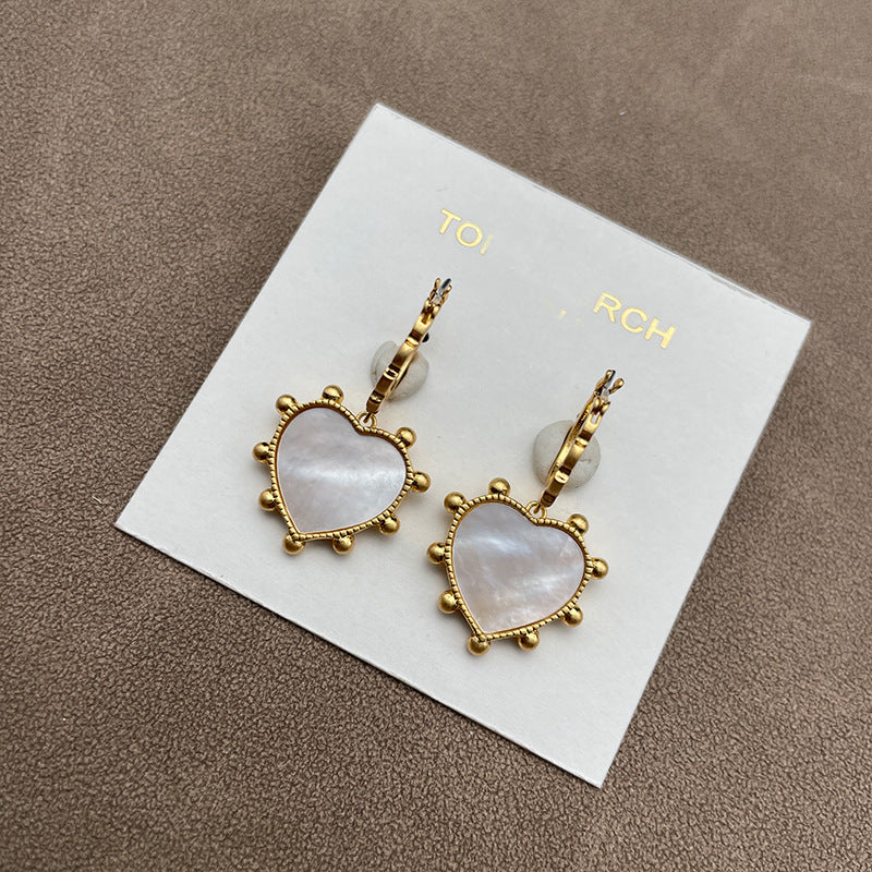 Both earrings laid side-by-side on a soft, neutral background (light gray velvet), showcasing the heart charm and mother of pearl drop in clear detail.