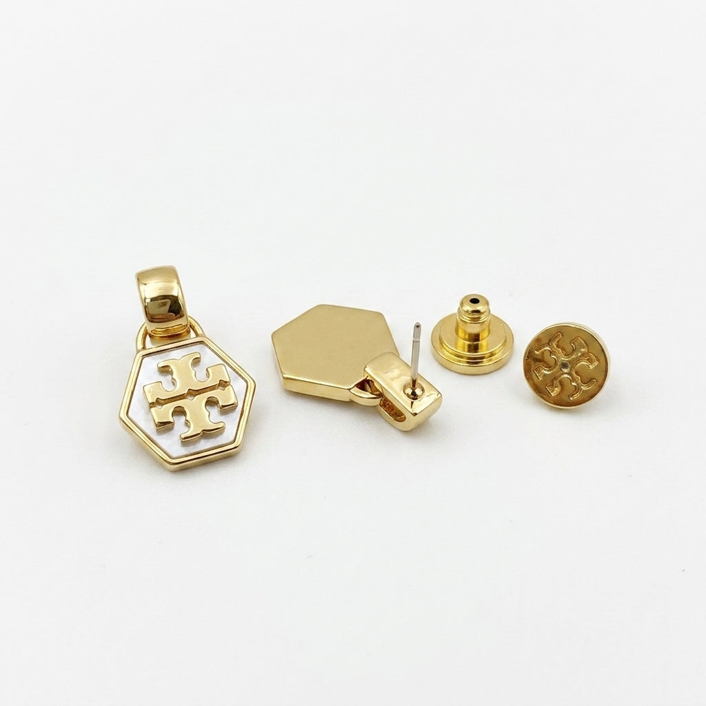 Gold-toned jewelry set featuring a hexagonal pendant with a white monogram logo, a matching hexagonal stud, a round matching stud, and a butterfly back, displayed on a clean white background.
