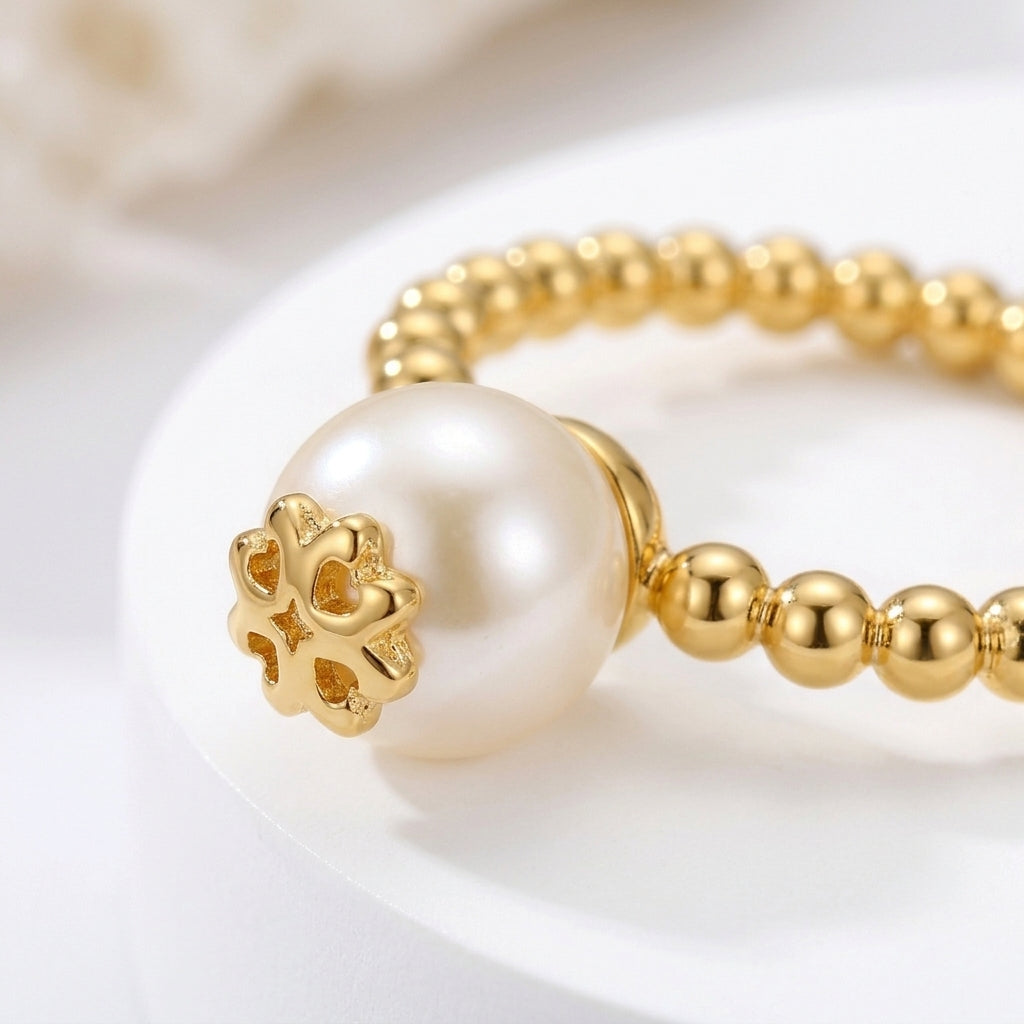 A gold beaded bracelet featuring a large white pearl and a decorative gold flower clasp, displayed on a white surface.
