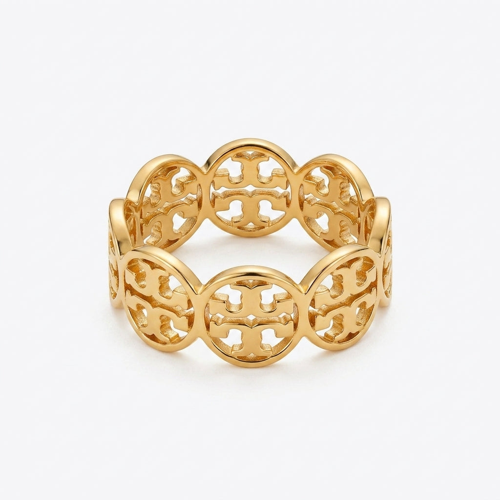 A gold-tone filigree bangle bracelet with a repeating interlocking monogram pattern, shown on a light gray background.