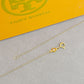 Gold necklace with a clasp on a gray surface with Tory Burch branding in the background.