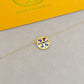 Gold necklace with a round pendant on a gray surface, with 'Tory Burch' branding in the background.