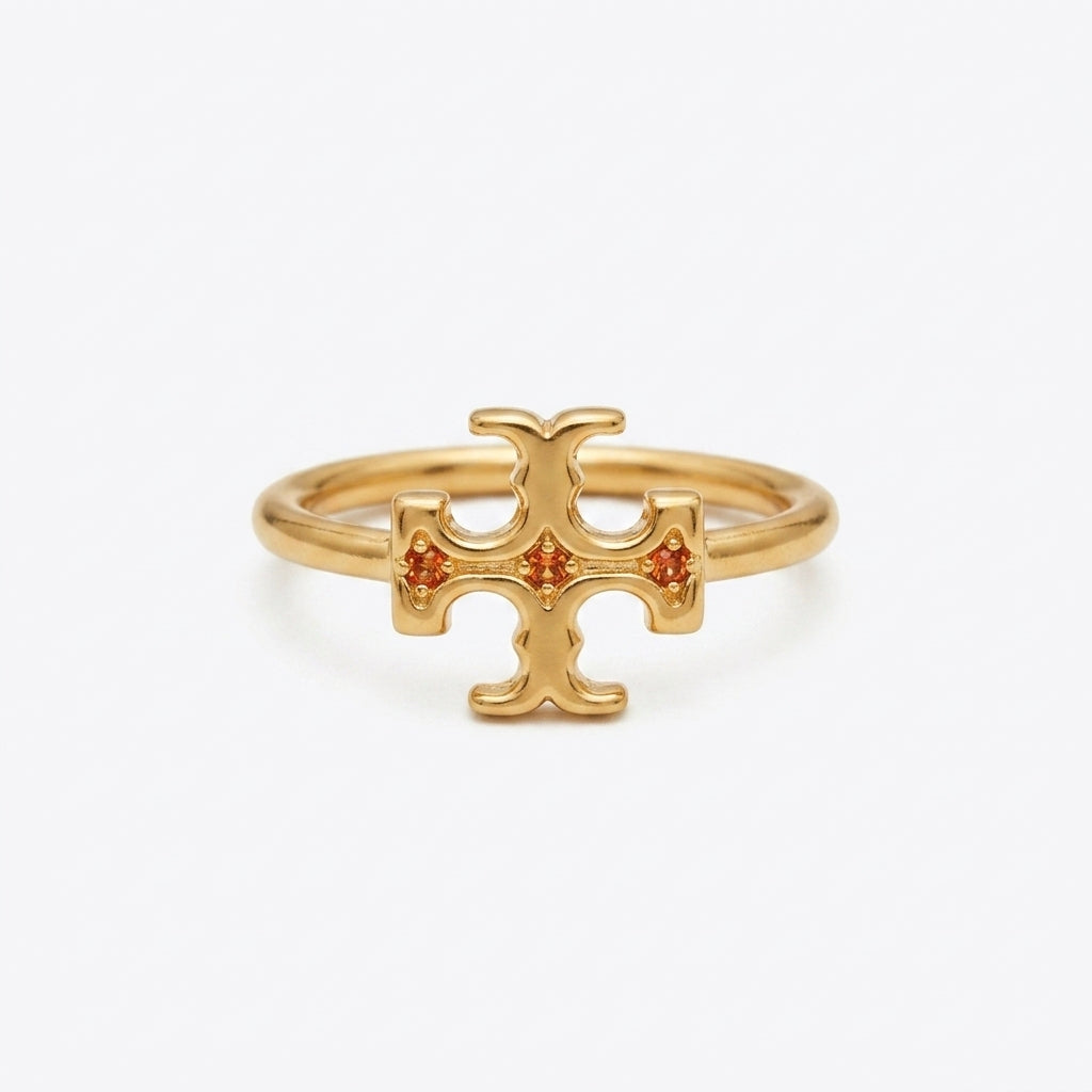 A gold ring featuring a stylized cross or T-shaped emblem with three small orange gemstones set into the center, photographed on a clean white background.