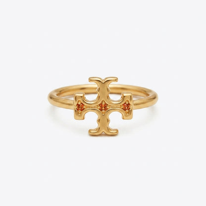 A gold ring featuring a stylized cross or T-shaped emblem with three small orange gemstones set into the center, photographed on a clean white background.