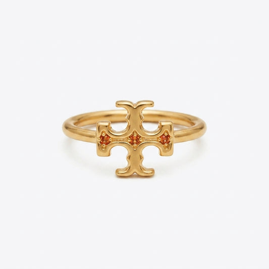 A gold ring featuring a stylized cross or T-shaped emblem with three small orange gemstones set into the center, photographed on a clean white background.