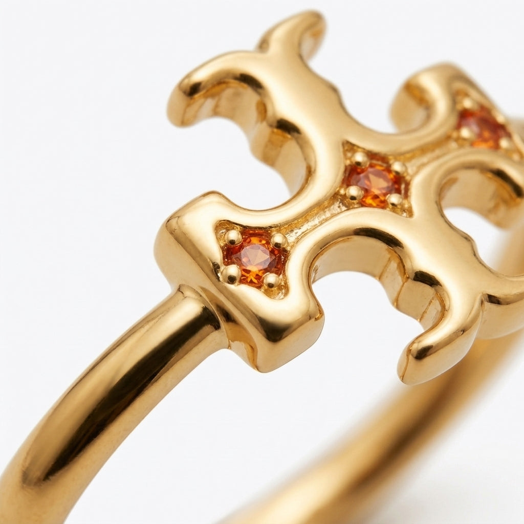 Gold ring with a stylized openwork cross or crown-like top set with small round orange gemstones, photographed close up on a white background.