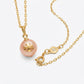 A gold chain necklace featuring a round, pale pink pearl pendant with a gold monogram logo, displayed on a clean white background.
