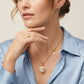 A close-up lifestyle shot of a woman wearing a delicate gold chain necklace with a white pearl pendant featuring a gold star design, paired with a gold ring on her finger and a light blue satin shirt.