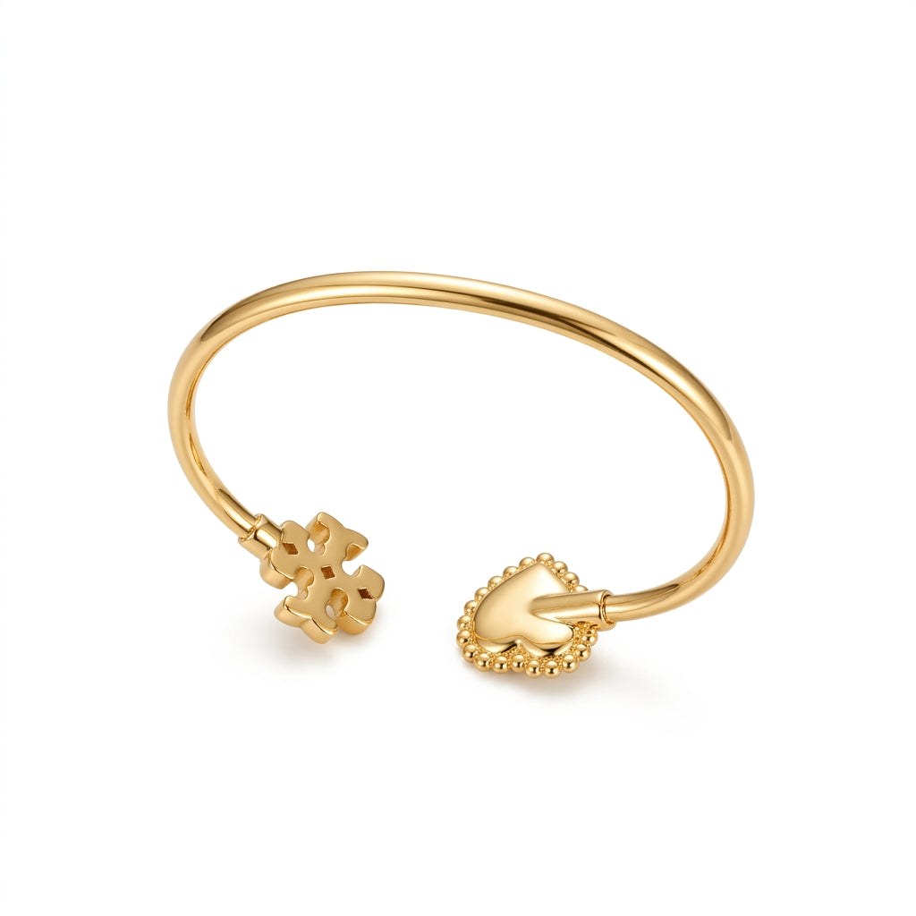 A gold-plated open cuff bangle bracelet featuring a small flower charm on one end and a heart-shaped bead border charm on the other, displayed on a clean white background.