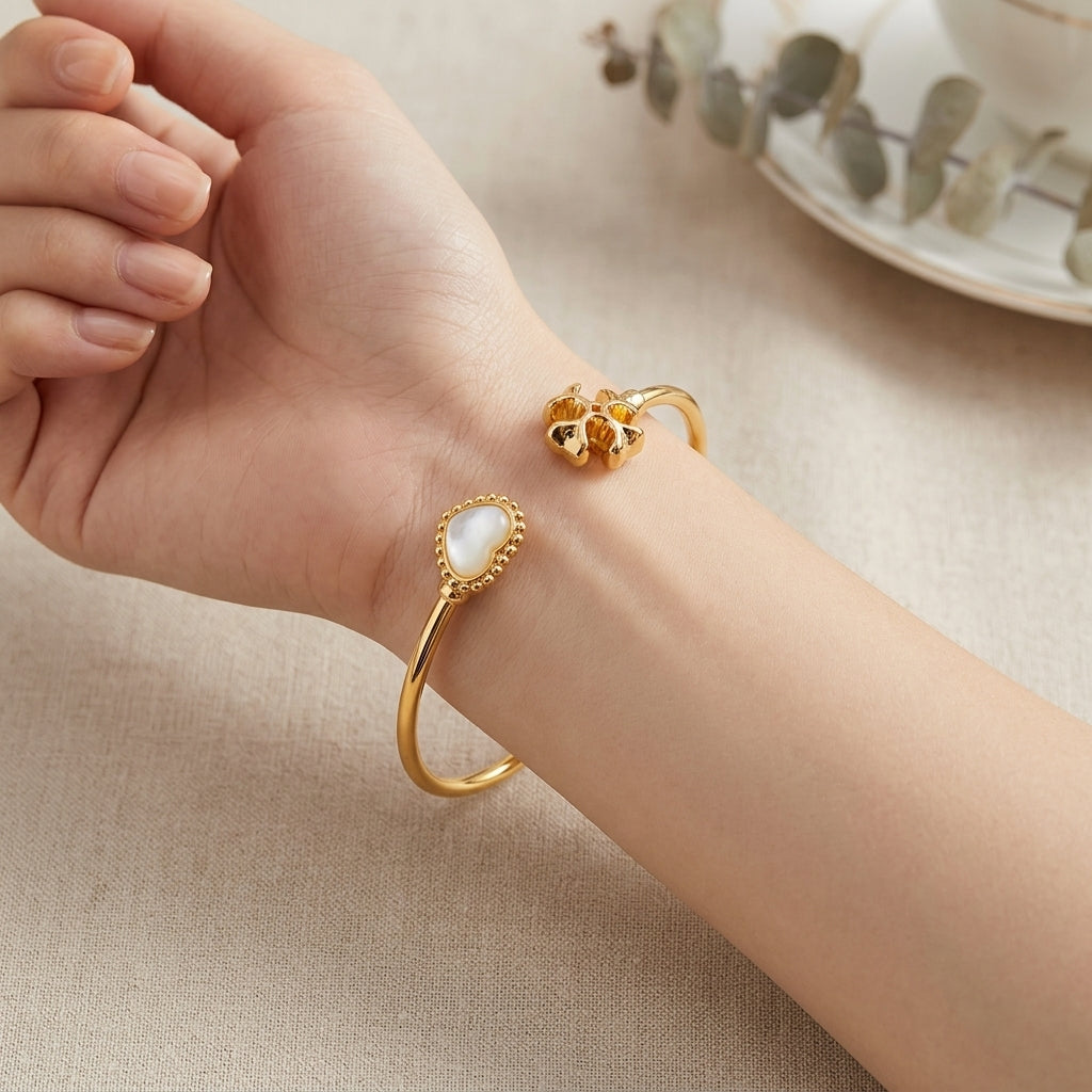 A close-up of a person's wrist wearing two gold-toned bangle bracelets. One bracelet features a smooth oval white pearl-like center, while the other has a textured gold floral or butterfly motif.