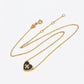 A delicate gold chain necklace featuring a small heart-shaped pendant with a black center and a gold monogram logo, displayed on a clean white background.
