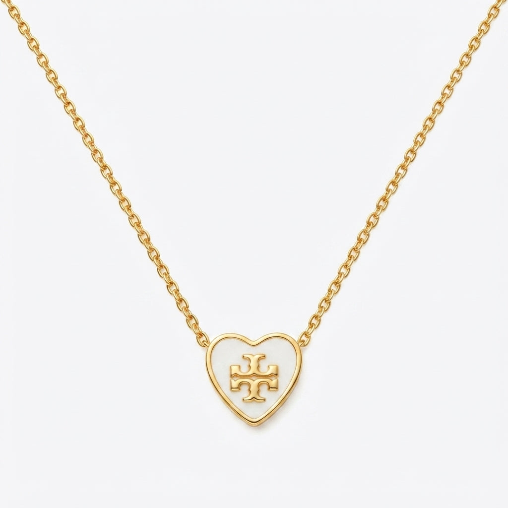 A gold heart-shaped pendant necklace with an open heart design and a central monogram logo, suspended from a delicate gold chain against a light gray background.