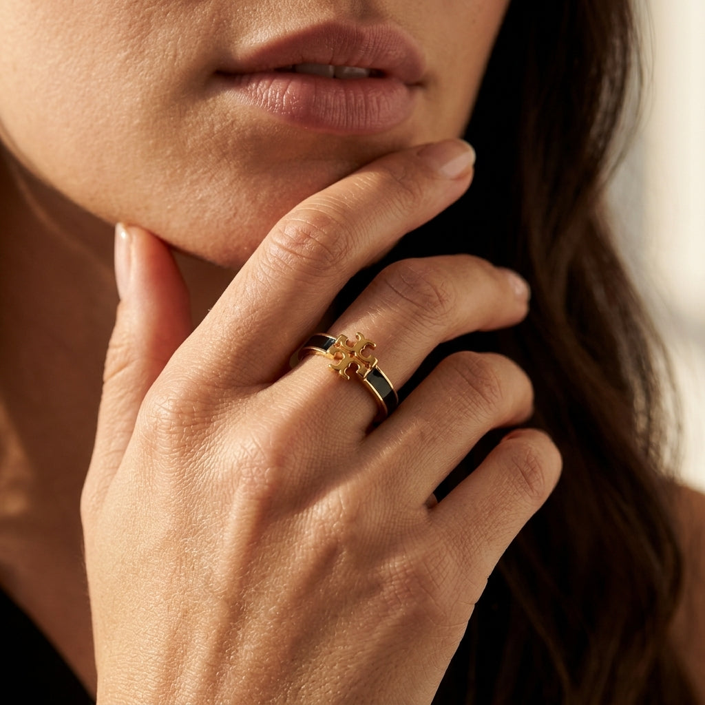 A close-up lifestyle shot of a model's hand resting near her chin, wearing a gold ring with a small yellow flower-like center and black bands.