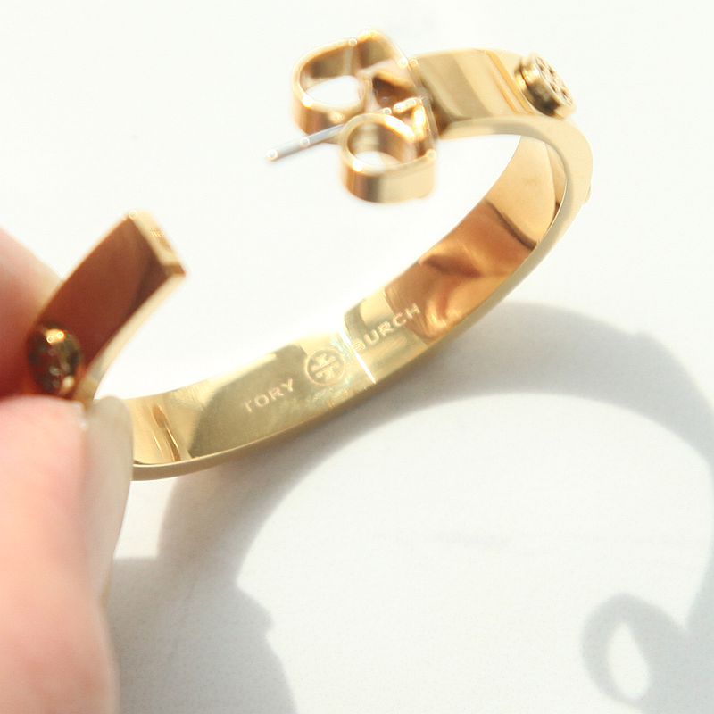 Gold-toned open cuff bracelet with a matching stud earring, held by a hand against a white background. The inside of the bracelet is engraved with 'TOKYOMURCH'.