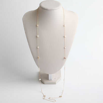 A delicate gold chain necklace with small white pearl-like beads spaced along the chain, displayed on a cream-colored jewelry bust against a light gray background.