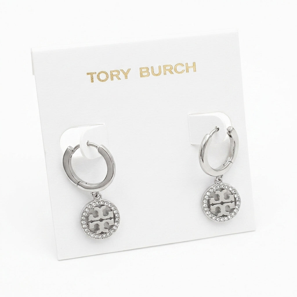 A pair of silver-tone Tory Burch hoop earrings with circular logo charms, displayed on a white branded card.