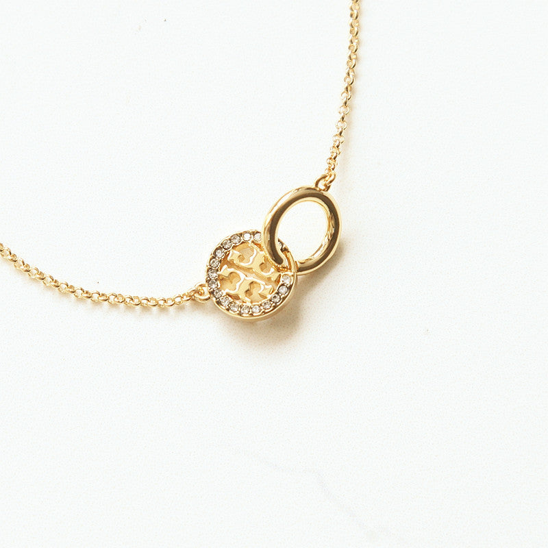 A gold chain necklace featuring a double-ring pendant, with one ring detailed in small clear stones and the center featuring an openwork gold pattern, photographed on a clean white background.