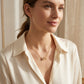 Model wearing a single necklace in a natural setting (window light or café). Soft natural light creates a subtle sparkle. Atmosphere is relaxed, elegant, and wearable.