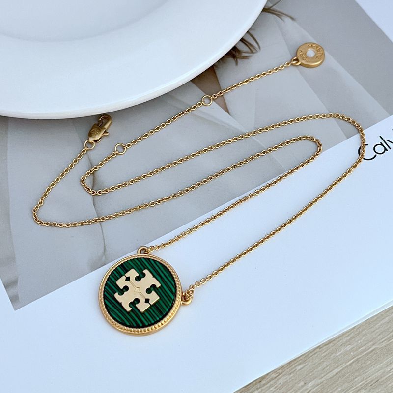 Gold necklace with a green and gold pendant on a white surface