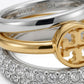 Close-up of a Tory Burch ring featuring a gold and silver double-band design, a gold monogram logo, and a pavé-set silver band with clear stones.