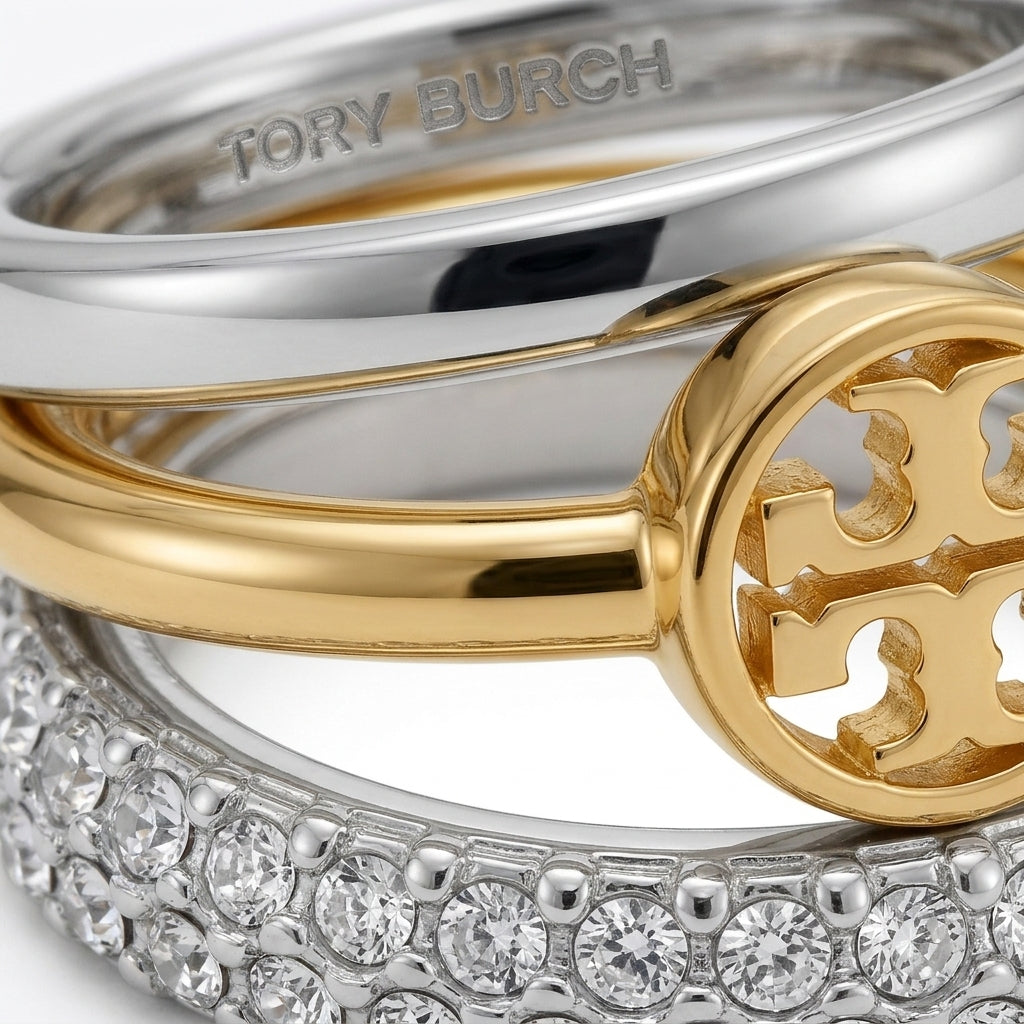 Close-up of a Tory Burch ring featuring a gold and silver double-band design, a gold monogram logo, and a pavé-set silver band with clear stones.