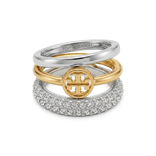 A stack of three Tory Burch rings on a white background. The top ring is silver with 'TORY BURCH' engraved inside.