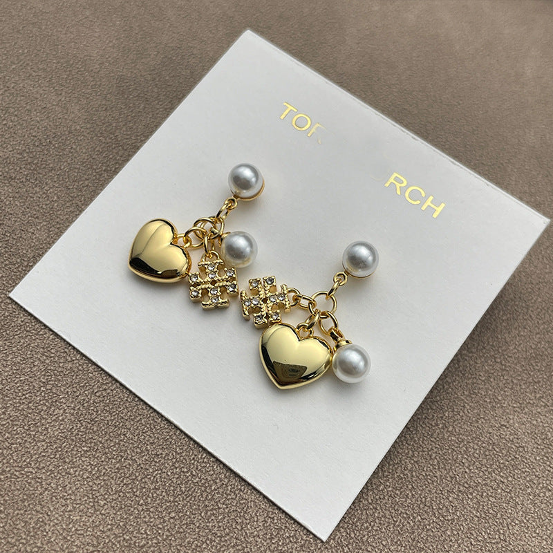 Close-up focused on the charm cluster, highlighting each element: crystal sparkle, heart shape, pearl luster, and engraved T logo.