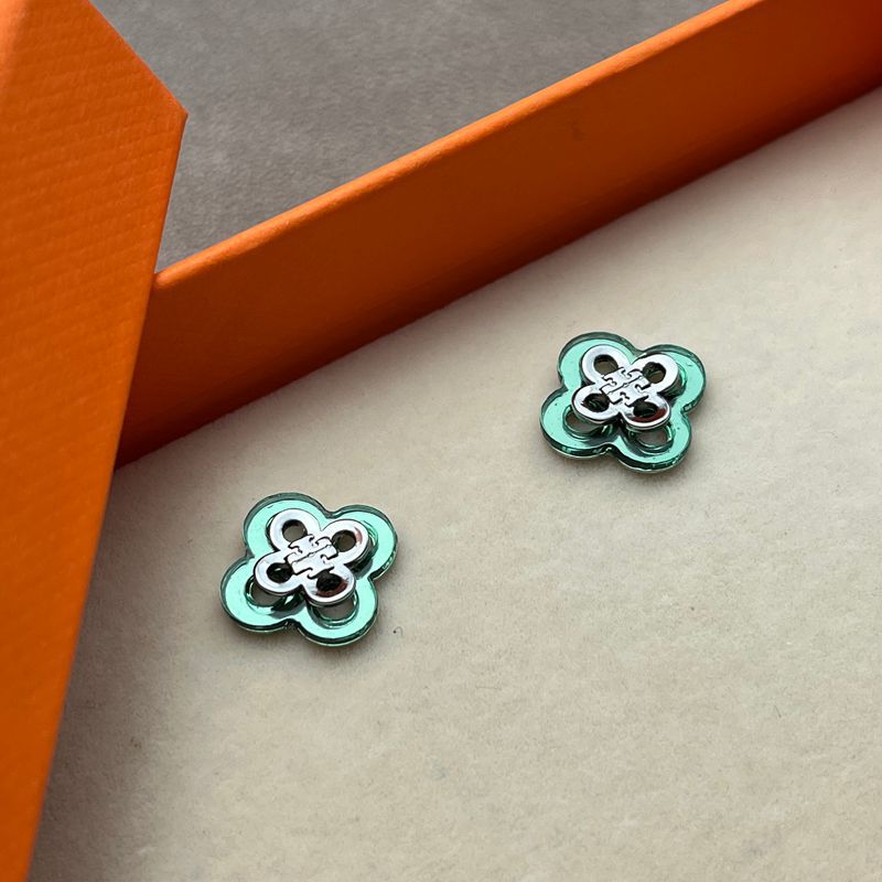 Both earrings displayed face-up on a light, textured background (like linen or soft suede), highlighting the clover shape and engraved detailing.