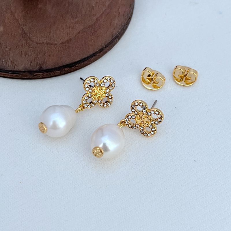 Extreme macro shot focusing on the intricate sculpting of the four-leaf clover charm and the flawless surface of the pearl drop, highlighting Tory Burch's craftsmanship.