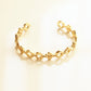 A gold chain bracelet with geometric, faceted links, displayed on a clean, light beige background with a soft reflection.