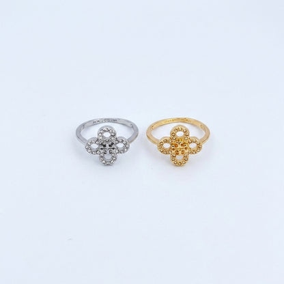 Two small flower-shaped rings on a plain white background, one in silver and one in yellow gold. The silver ring has clear stones, and the gold ring has textured openwork detailing.