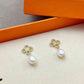 Both earrings displayed hanging freely against a light, soft-focus background, showing the clover charm above the pearl drop.