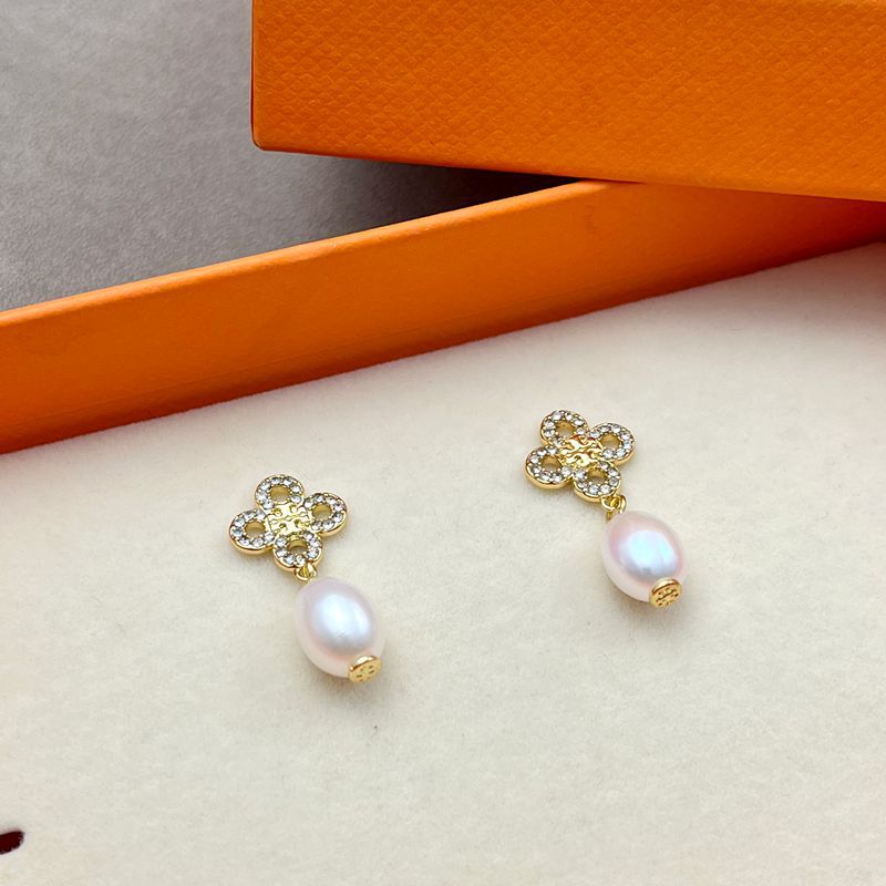 Both earrings displayed hanging freely against a light, soft-focus background, showing the clover charm above the pearl drop.