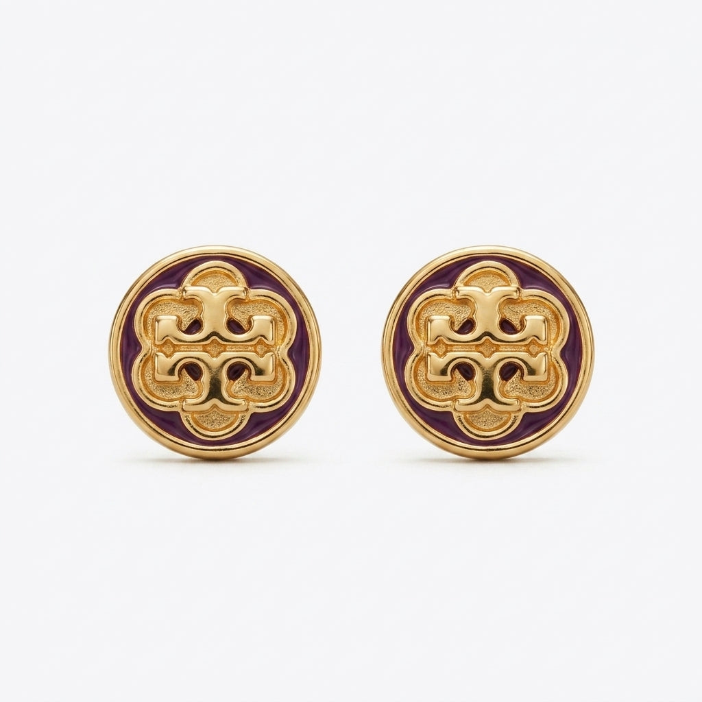A pair of round gold-tone stud earrings featuring an intricate interlocking monogram design in gold over a deep purple enamel background, set against a clean white studio backdrop.