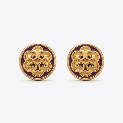 A pair of round gold-tone stud earrings featuring an intricate interlocking monogram design in gold over a deep purple enamel background, set against a clean white studio backdrop.