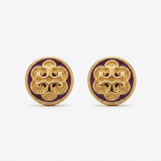 A pair of round gold-tone stud earrings featuring an intricate interlocking monogram design in gold over a deep purple enamel background, set against a clean white studio backdrop.