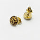 A pair of gold stud earrings on a white background, with one earring showing the front face featuring a raised quatrefoil logo and the other showing the side profile with the post and backing.