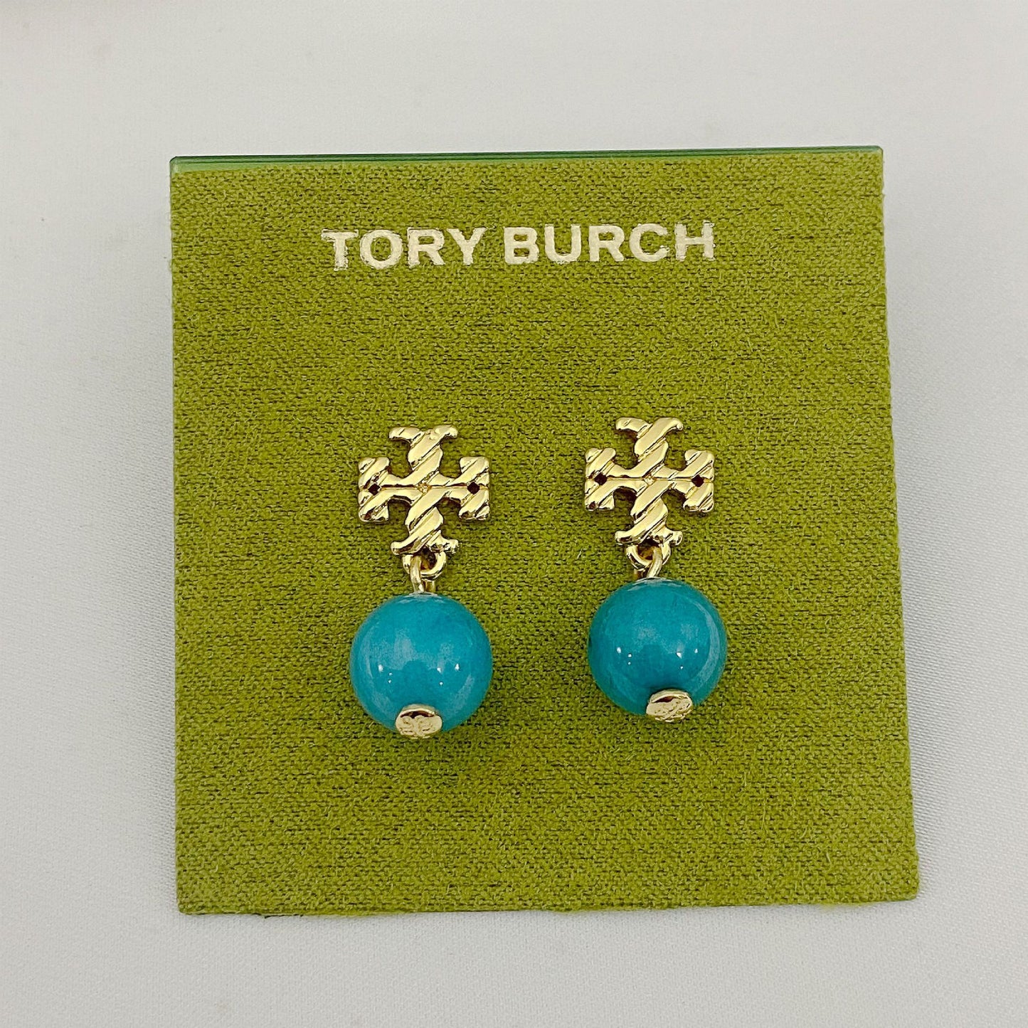Tory Burch earrings with turquoise beads and gold accents on a green card.