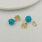 Gold and turquoise earrings on a light gray surface