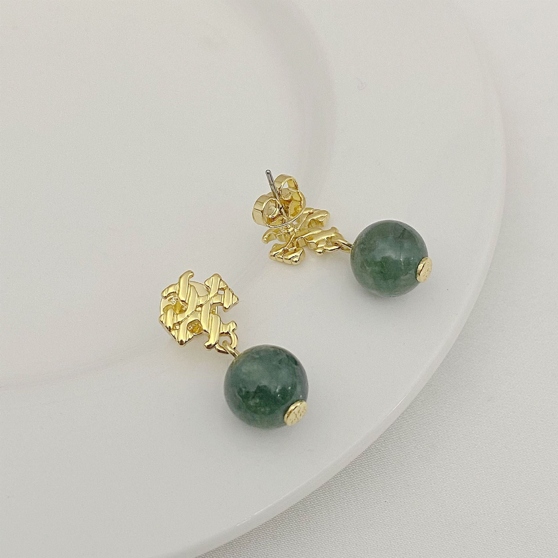 Pair of earrings with green beads and gold accents on a white background