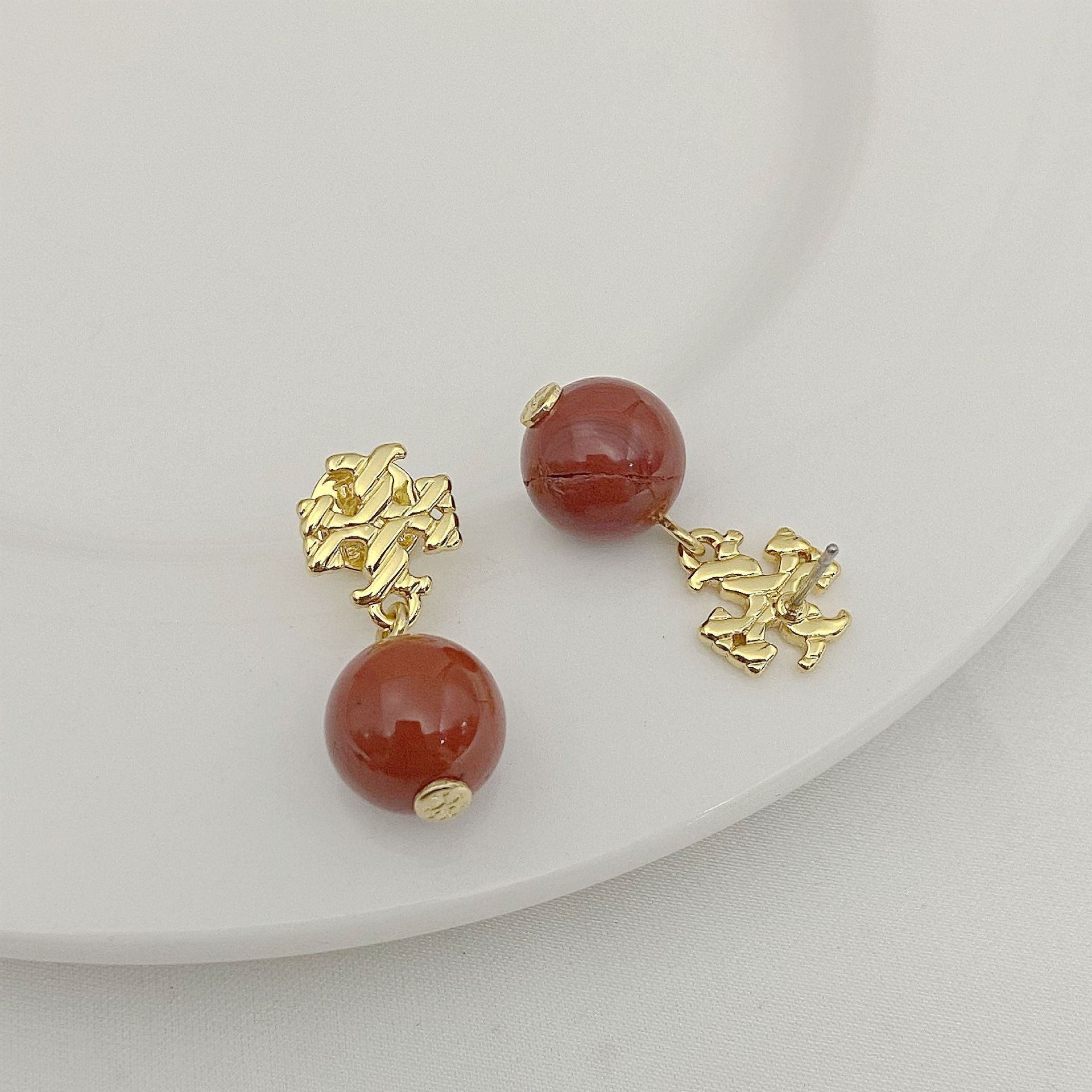 Pair of earrings with red beads and gold accents on a white plate.
