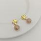 Pair of gold earrings with pink beads on a white plate.