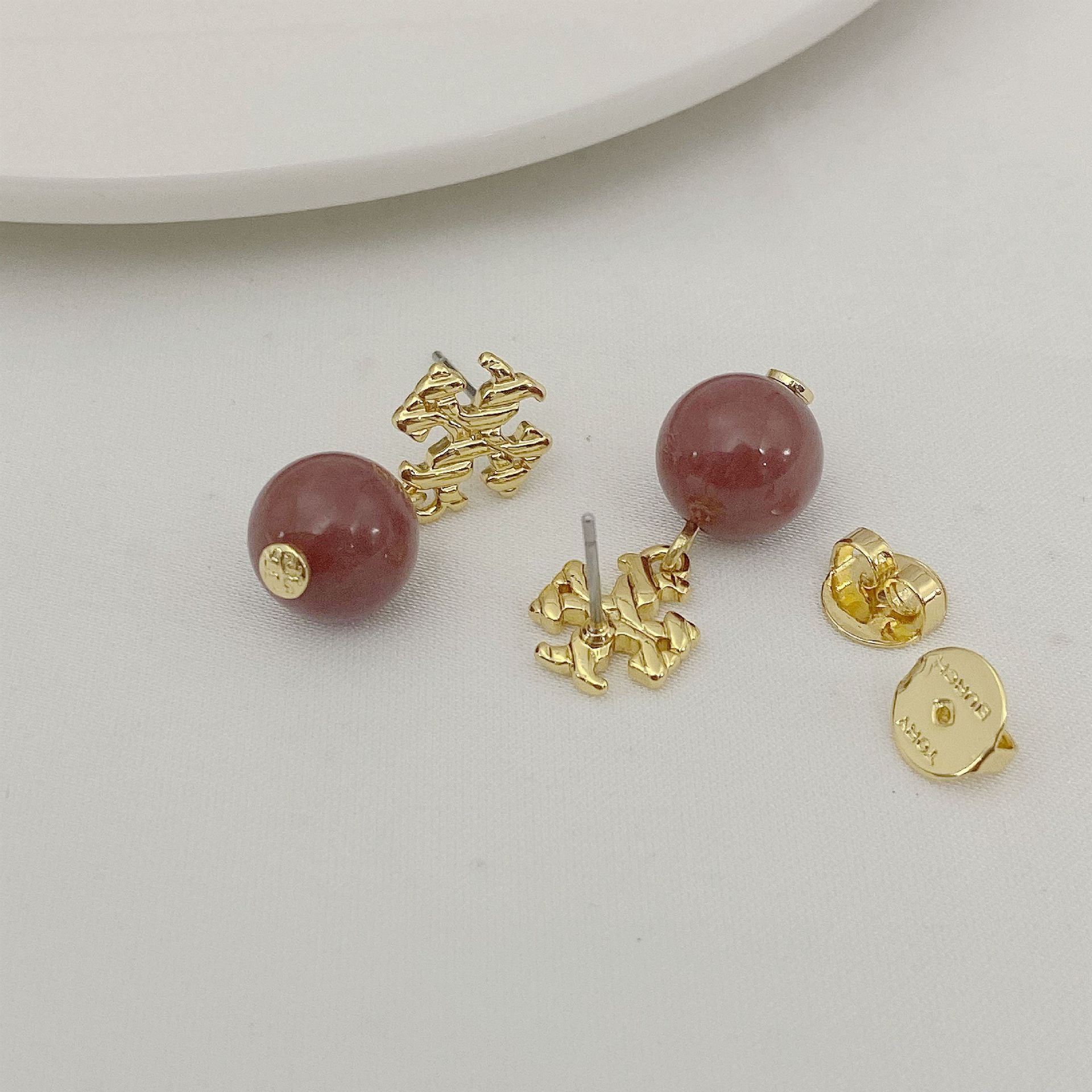 Gold earrings with red gemstones on a light gray background